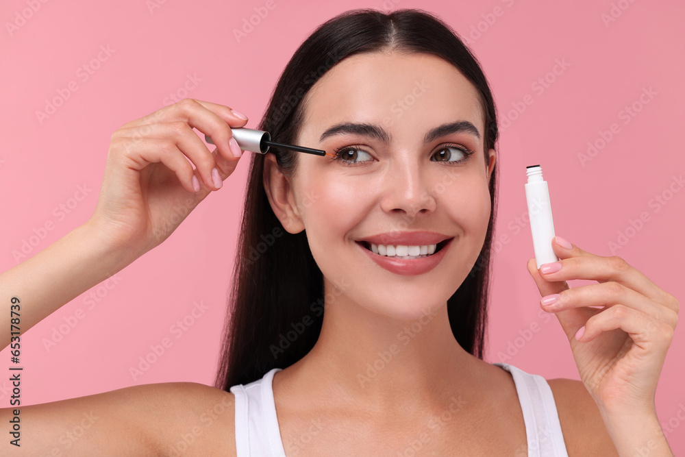 Poster Beautiful woman applying serum onto her eyelashes on pink background. Cosmetic product