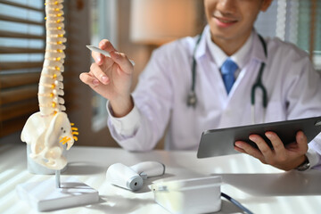 Orthopedists holding digital tablet and pointing at model. Concept of osteoporosis, back pain,...