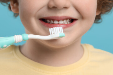 Cute little boy brushing his teeth with plastic toothbrush on light blue background, closeup