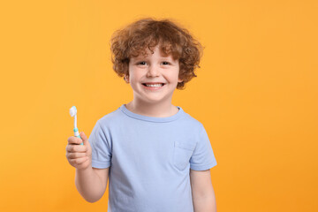 Cute little boy holding plastic toothbrush on yellow background