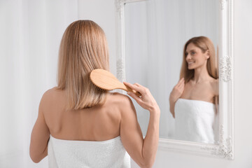 Obraz premium Woman after shower brushing her hair near mirror in room