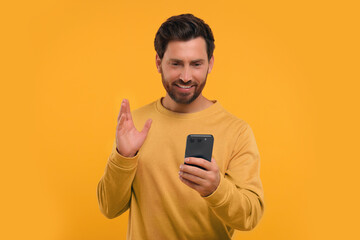 Handsome bearded using smartphone on orange background