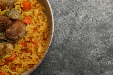 Delicious pilaf with meat on grey textured table, top view. Space for text