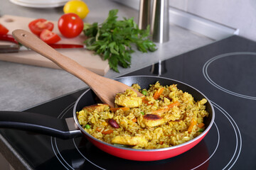 Tasty rice with meat and vegetables in frying pan on induction stove