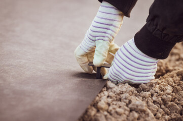 A person hammers a plastic stake into the ground to hold the agrofibre on the ground.