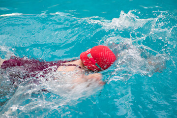 Young girl in goggles and cap swimming front crawl stroke style in the blue water pool