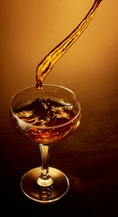 Top view photo of pouring whiskey, rum, brandy or gin to high glass over golden gradient background.