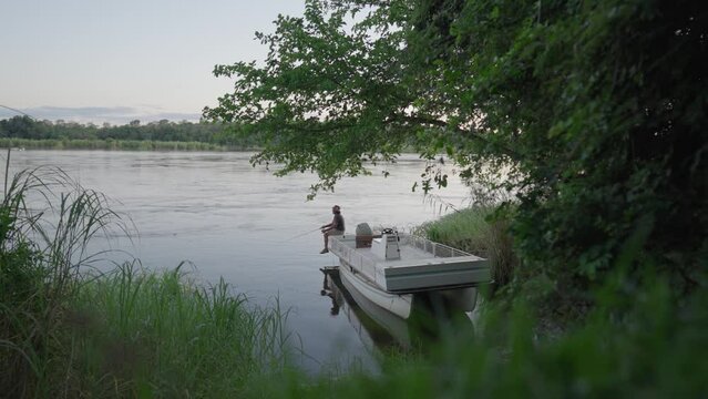 Man fishing off a parked boa on the edge of the flowing Zambezi river