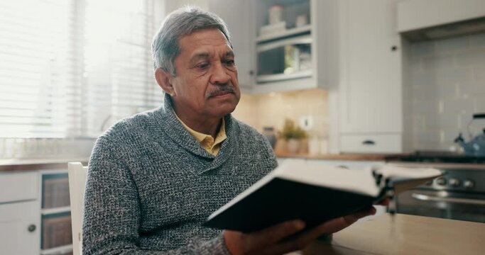 Senior man, reading and bible study in home kitchen for spiritual growth, knowledge or learning with faith. Elderly person, book and religion with thinking, mindfulness or peace for connection to God