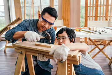 Happy Asian father and son work as a woodworker and carpenter. Father teaching his son to hammer...