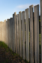 Wooden fence with wide slats and a marked and beautiful texture and a gap between them undulating in perspective and giving the sensation of depth with grass and a garden area in the background