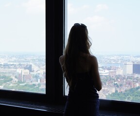 A girl looks out the window at the panorama of the city of Boston. Silhouette of a girl
