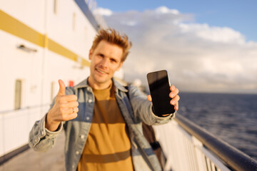 Under the setting sun on a ship, a joyful young man immerses himself in his smartphone during a...