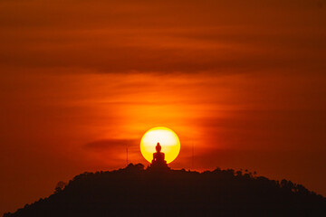 Stunning red sky sunset the round sun is on the back of Phuket big Buddha on the high mountain. .landmark of Phuket island..Phuket big Buddha in circle of the sun in red sky..red sky background.