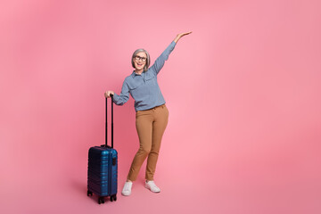 Full length photo of cheerful senior lady trendy clothes rejoice resort abroad demonstrate empty space isolated on pink color background