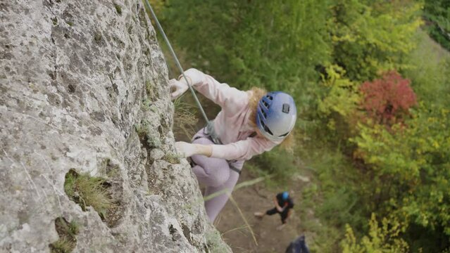 Strong female rock climber climbs a steep cliff in a helmet with a rope