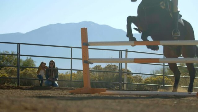 Mother and daughter watching horse make jump - slow motion
