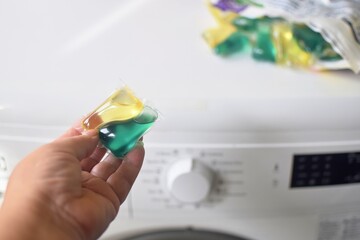 The woman took a capsule of washing powder and is about to put it in the washing machine.  Washing clothes.