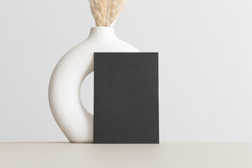 Black invitation card mockup with a pampas decoration on the beige table. 5x7 ratio, similar to A6,...