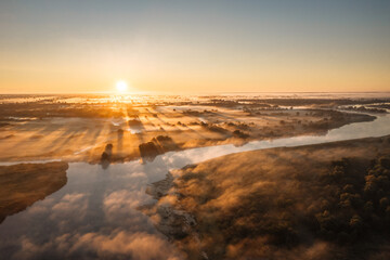 Morning sunrise on the big river. The photo was taken from a drone, there is beautiful fog and a blue winding river below.  View of a field next to a river.