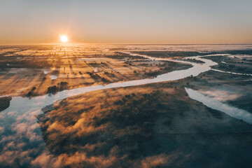 Morning sunrise on the big river. The photo was taken from a drone, there is beautiful fog and a blue winding river below.  View of a field next to a river.