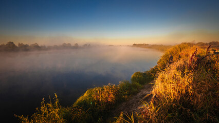 Morning sunrise on the big river. The photo was taken from a drone, there is beautiful fog and a blue winding river below.