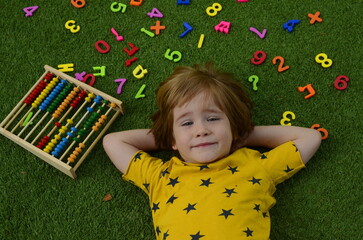 The boy studies the numbers. The child lies on the grass, there are numbers around. Concept:...