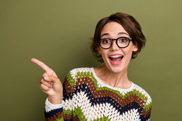 Photo of excited funky girl dressed striped clothes eyewear pointing finger empty space isolated green color background