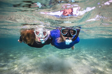 Two snorkelers in clear water looking at the camera floating on the water surface - obrazy, fototapety, plakaty