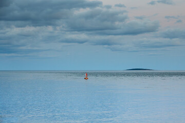 Naklejka premium Red and white buoy in the ocean with an island in the distant background seen during a cloudy evening blue hour, Bass Harbor, Maine, USA