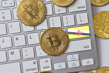 national flag of brunei on the keyboard with bitcoin coins on a grey background.