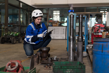 Fototapeta na wymiar Female warehouse worker working and using digital tablet inspecting quality parts of machine in industry factory, wearing safety uniform, helmet