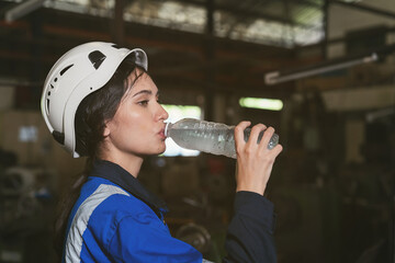 Female factory worker drinking water in break time in factory. Woman worker working and wearing...