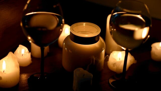 Two glasses of white wine and candles in the dark. The wind blows out the candles. Close-up. Romantic dinner