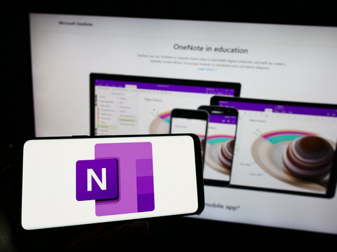 Stuttgart, Germany - 09-21-2023: Person holding cellphone with logo of note-taking software Microsoft OneNote on screen in front of company webpage. Focus on phone display.