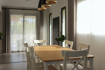 Stylish dining room with pendant light fixtures, empty table and a big full length windows. Copy space, background.
