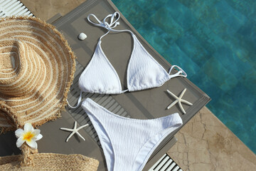 Swimming pool essentials concept. Bikini bathing suit, beach bag and broad brim straw hat by the...