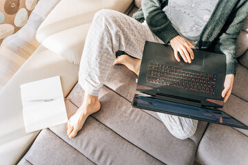 A woman in home clothes with a laptop, next to her is a notebook and a pen