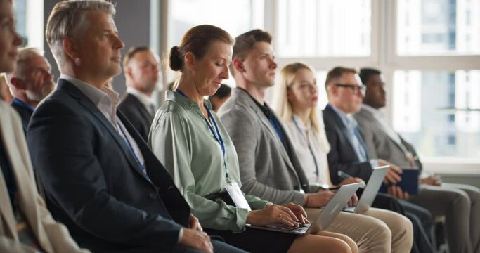 Senior Caucasian Woman Sitting in Crowded Audience at a Business Conference. Female Top Manager Smiling, Using Laptop Computer. Specialist Watching Presentation About Investing In Innovative Startups.