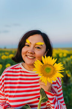 Smiling woman with sunflower petals on eyebrows in field
