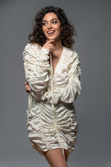 Cheerful young woman in white draped dress posing on gray background