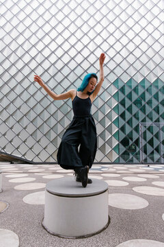 Young dancer dancing on circular concrete seat in front of modern building