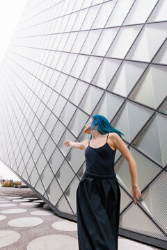 Woman with dyed blue hair dancing near modern building