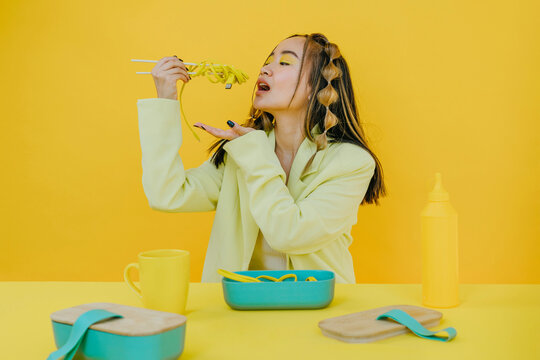 Young woman having wired noodles against yellow background