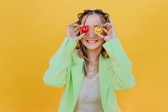 Smiling woman covering eyes with smileys against yellow background