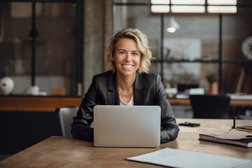 A smiling businesswoman working on her laptop in the office. - obrazy, fototapety, plakaty