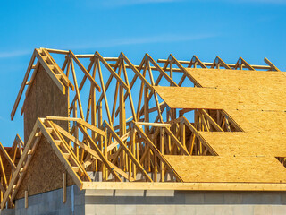 Wooden roof trusses and particle board panels on top of a single-family suburban house under construction on a sunny morning in southwest Florida