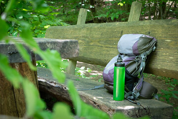  Hiking backpack on wooden bench in the forest, green water bottle with water - 653277949