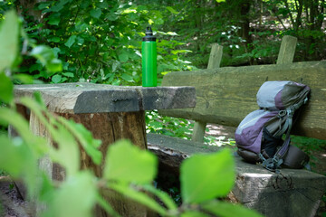  Hiking backpack on wooden bench in the forest, green water bottle with water - 653277953