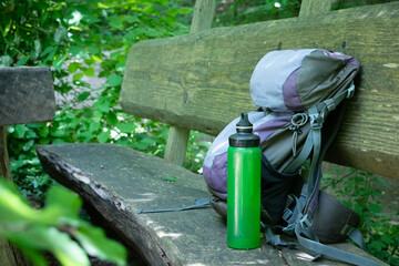  Hiking backpack on wooden bench in the forest, green water bottle with water - 653277968